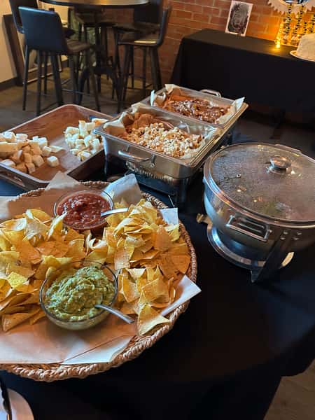 Buffet spread with tortilla chips, fresh guacamole and salsa, queso dip, mac and cheese, and bread cubes in a casual restaurant setting