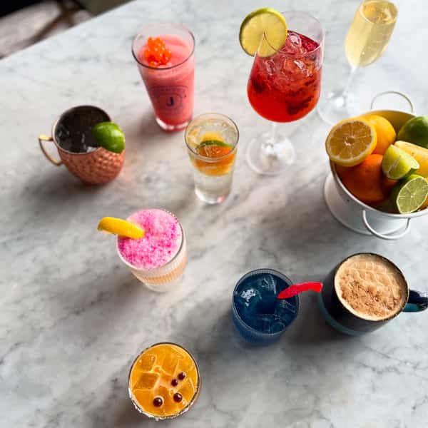 assorted colorful craft cocktails with citrus garnishes and fresh fruit on a marble bar table, including spritz, margarita, and espresso martini