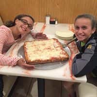 two young girls smiling at a table with a square cheese pizza