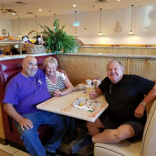 three people sitting at booth smiling for picture