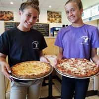 two female employees holding pizzas