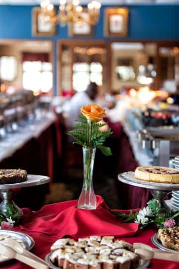 Single orange rose inside a vase and desserts on display on a table with a red table cloth