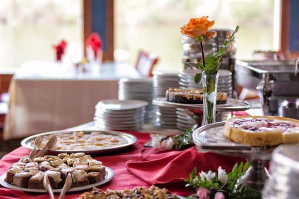 Assorted desserts and pastries set up on table with a red table cloth and a yellow rose centerpiece