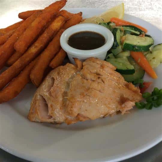 Piece of salmon with a side of steamed vegetables, sweet potatoes fries and dipping sauce
