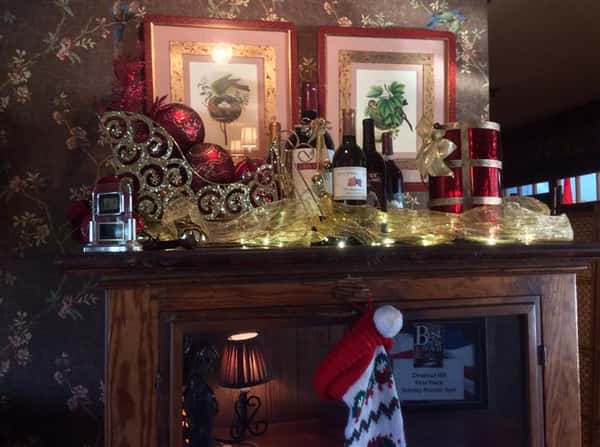 Fireplace mantle decorated with a variety of decorations including a sleigh, wine bottles and a stocking
