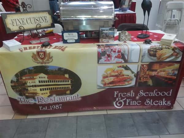 Picture of table set-up with a sign saying "Fine Cuisine" on-top of a banner reading "Fresh Seafood and fine steak"