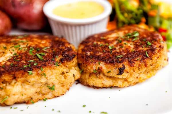 Two crab cakes dusted in parsley with a side of dipping sauce