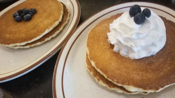 Fluffy pancakes on white plate topped with whipped cream and blueberries