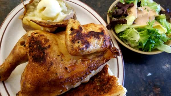 Golden browned whole chicken on white plate with baked potato and salad