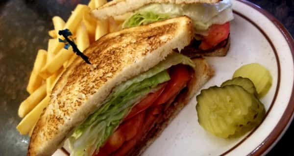 Toasted BLT on white plate with toothpick in middle next to fries