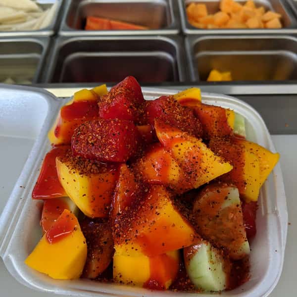 Mixed fruit cup with mango, cucumber, and watermelon topped with chamoy and chili powder in a foam container.