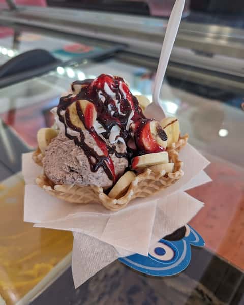 A waffle bowl filled with chocolate ice cream, sliced bananas, whipped cream, and a drizzle of strawberry and chocolate syrup.