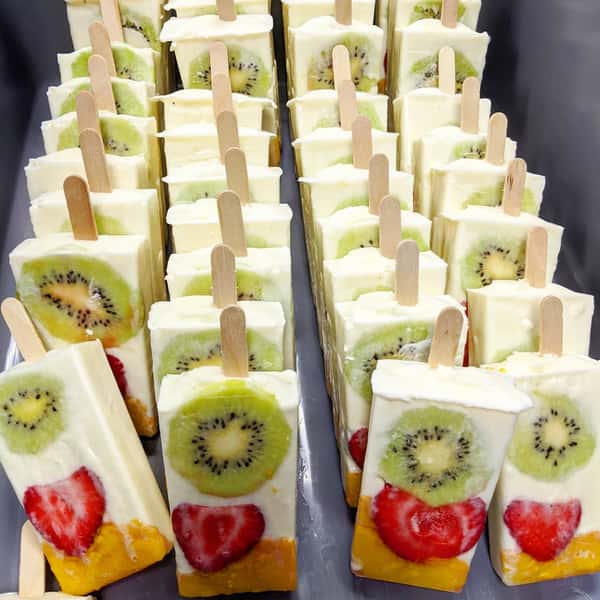 A collection of frozen fruit popsicles with layers of kiwi, strawberry, and mango, on wooden sticks.