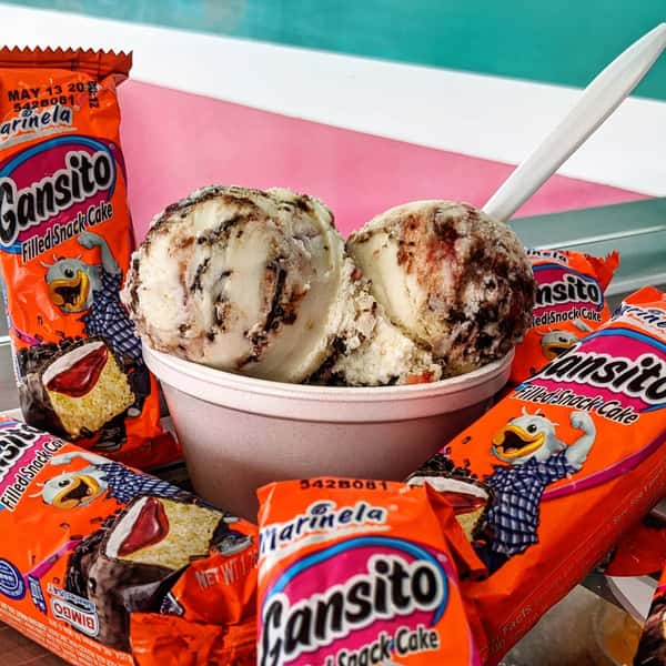 A bowl of ice cream topped with Gansito snack cakes, featuring swirls of chocolate and strawberry, with a spoon.