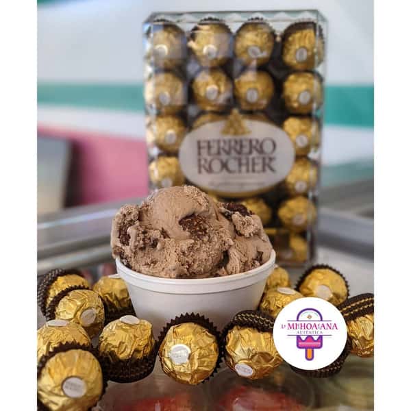 A bowl of chocolate ice cream with pieces of Ferrero Rocher chocolate, surrounded by multiple Ferrero Rocher chocolates and a logo in the foreground.