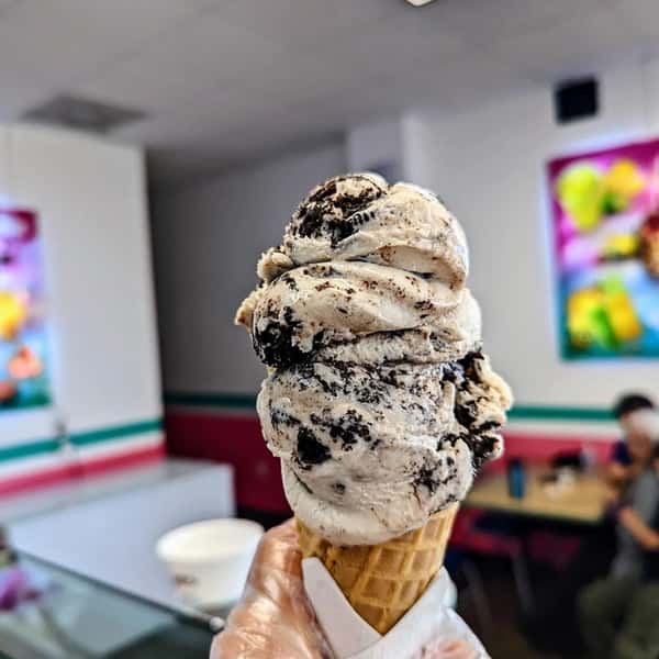 A cone of cookies and cream ice cream with two generous scoops topped with crushed cookies, served in a waffle cone.