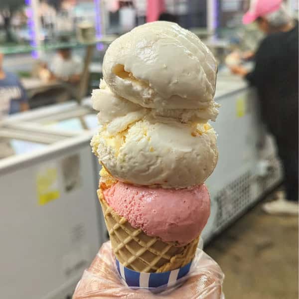 A cone with three scoops of ice cream: white, yellow, and pink, stacked on top of each other.