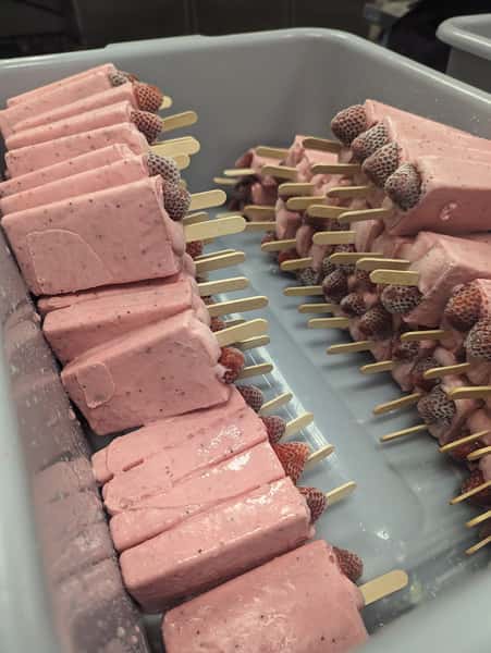 A tray filled with strawberry popsicles, each with a piece of fresh strawberry at the top, ready to be served.