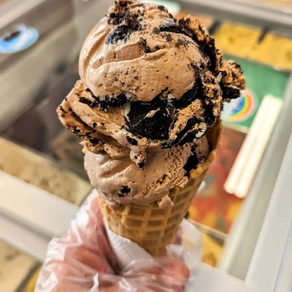 A chocolate ice cream cone with Oreo cookie pieces mixed in, served in a waffle cone.