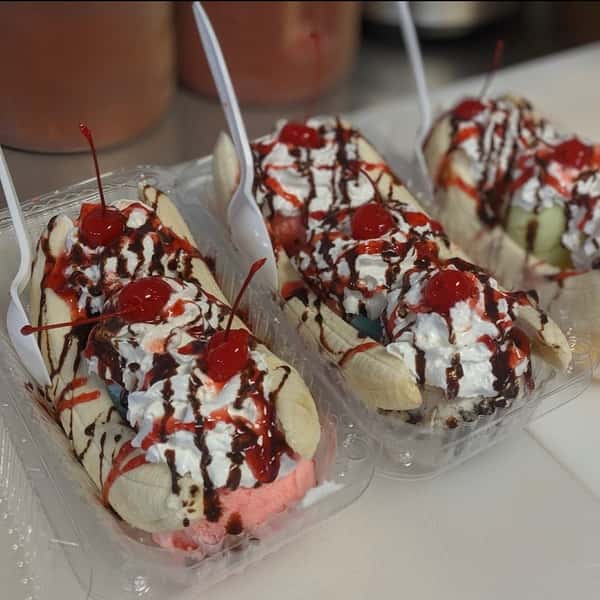 Banana split with whipped cream, chocolate syrup, cherry, and colorful sprinkles. Served in a plastic container.