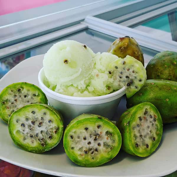 A bowl of prickly pear (sabra) sorbet surrounded by fresh, halved prickly pears with visible seeds.