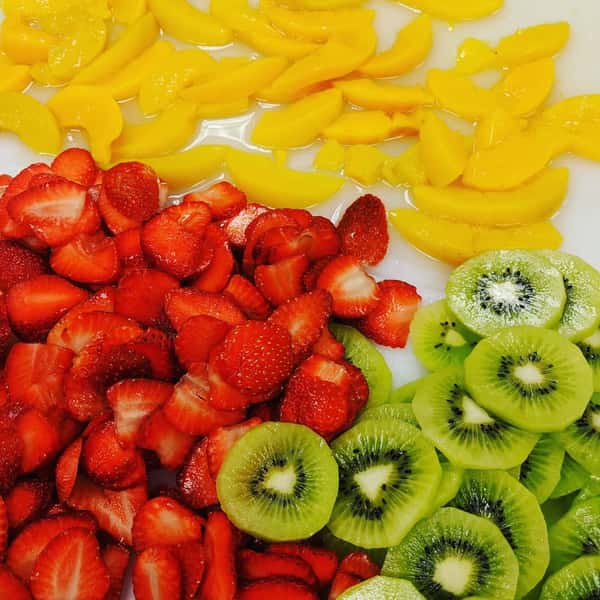 Freshly sliced strawberries, kiwi, and mango arranged in separate sections on a countertop, ready for use.