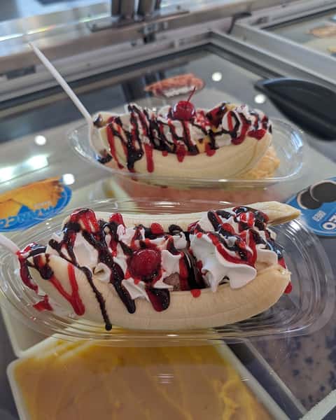 Two banana splits topped with whipped cream, cherries, and chocolate and strawberry syrup.