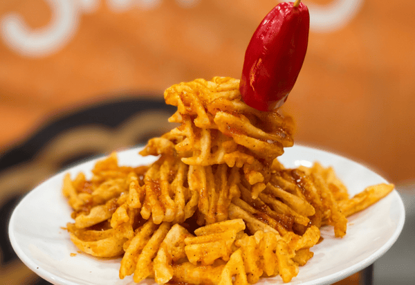 Crispy waffle fries tossed in bold seasoning and stacked with a red chili pepper garnish, served as a spicy loaded side dish.