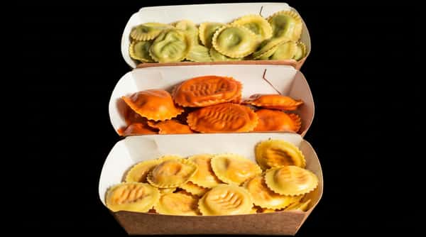 Three paper containers filled with different colored ravioli: green, orange, and yellow.