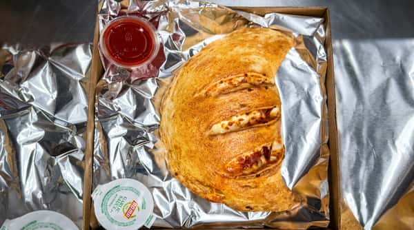 Toasted calzone with cheese filling, alongside small cups of red sauce and garlic sauce, in a foil-lined box.