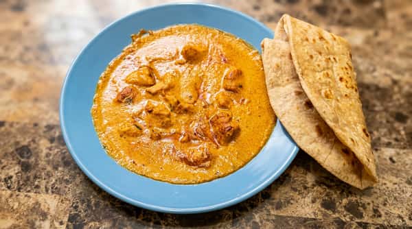 Chicken tikka masala with naan bread on a blue plate, on a marble table.