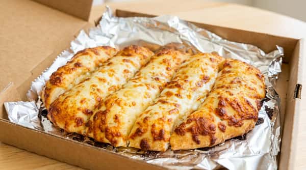 Cheesy breadsticks with melted, browned cheese in a foil-lined cardboard box.