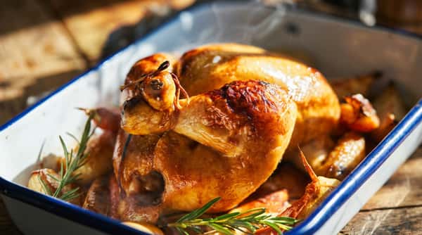 Roasted chicken in a blue baking dish with rosemary and potatoes, steam rising off of it.