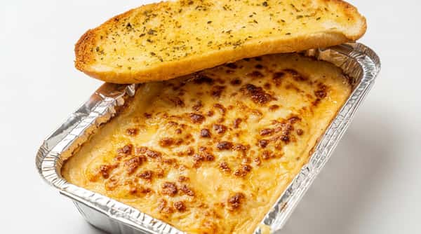 Baked macaroni and cheese with golden-brown crust in an aluminum foil tray, served with garlic bread stick.