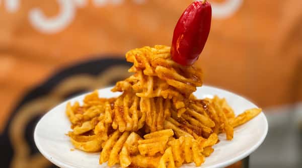 Crispy waffle fries piled high and seasoned with bold spices, topped with a bright red pepper for a playful appetizer presentation.