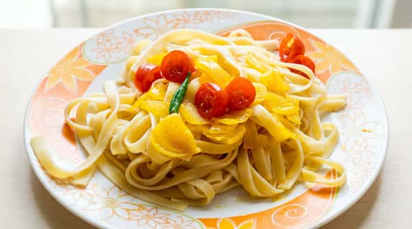 Fettuccine pasta with sautéed yellow bell peppers, cherry tomatoes, and a green chili on a floral plate.