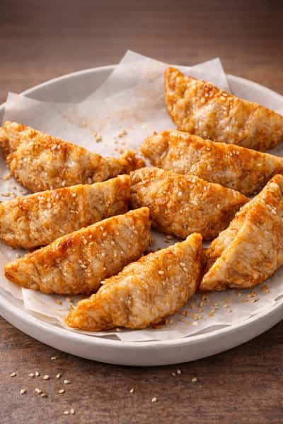 Plate of golden pan-fried dumplings with sesame seeds, crispy Asian-inspired appetizer.