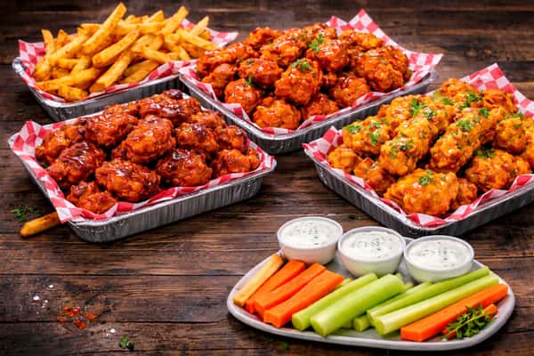 Restaurant platter with multiple wing flavors, crispy chicken tenders, fries, ranch dips, and fresh celery and carrots.