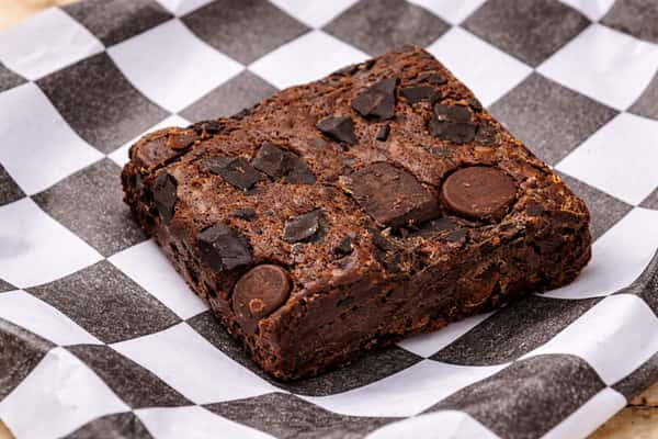 Rich chocolate brownie with chocolate chunks served on deli paper, classic dessert treat.