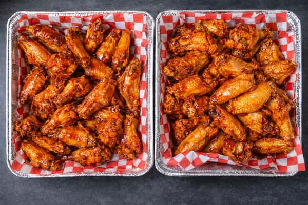 Two catering trays filled with crispy buffalo chicken wings served on red checkered deli paper.