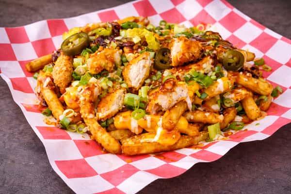 Loaded fries topped with crispy chicken, melted cheese sauce, jalapeños, and green onions on red checkered paper.