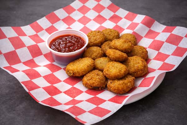 Golden fried pickle chips served on a plate with tangy dipping sauce and red checkered deli paper.