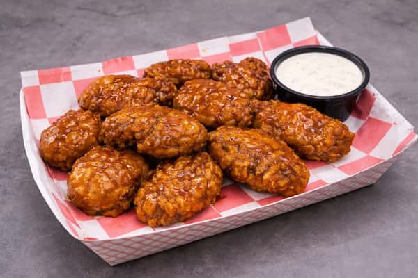 Seasoned dry-rub chicken wings with crispy coating served in a takeout container with ranch dipping sauce.