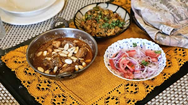 Delicious Indian meal featuring a hearty curry with almonds and fresh salad on a decorative mat.