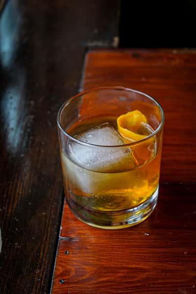 glass with large ice cube whiskey and orange cherry garnish
