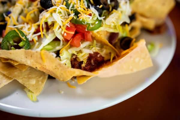 Loaded nachos topped with melted cheese, jalapeños, tomatoes, lettuce, black olives, and seasoned ground beef.