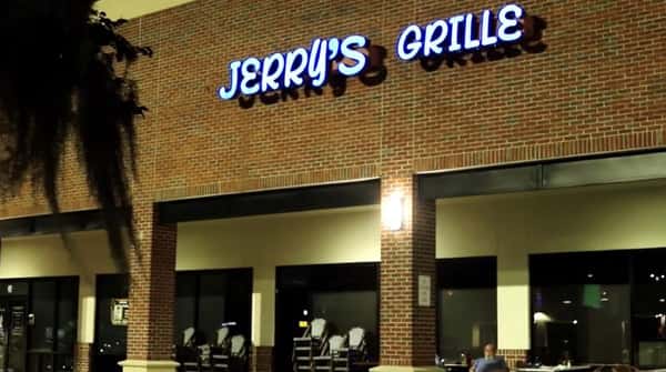 Jerry's Grille storefront at night featuring illuminated blue signage on a brick building with outdoor seating.