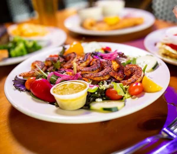 Blackened shrimp salad topped with mixed greens, cherry tomatoes, cucumbers, red onions, and a side of creamy dressing.