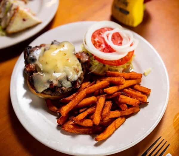 Cheeseburger with melted cheese, lettuce, tomato, and onion served with sweet potato fries on a white plate.