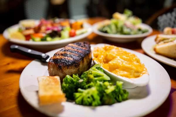 Grilled pork chop served with creamy mac and cheese, steamed broccoli, and a slice of garlic bread.